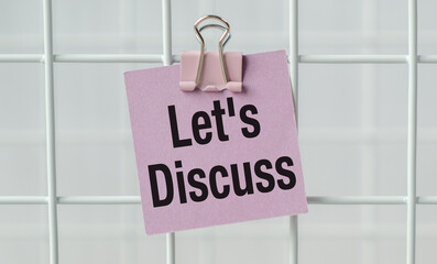 A pink sign that says Let's Discuss is hanging on a white metal fence