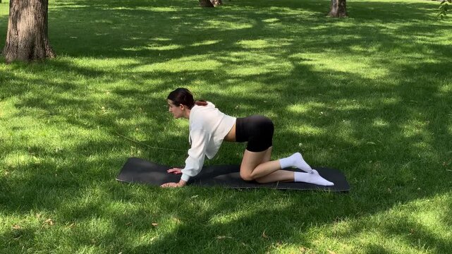 Caucasian fit female girl sport woman doing glute kickback exercise on yoga mat in green park butt workout for strong body fitness training yoga Pilates active healthy lifestyle lower body discipline