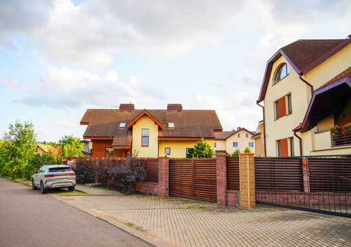House in suburban neighborhood. Two story suburb house with garage. Blossom landscape at family house. Fence of home at street with pavement road. Car parked on empty street in residential area. - Powered by Adobe