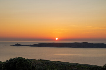Sun setting over Mediterranean sea with island silhouette, France, Corsica, Cargèse, 18 June 2025