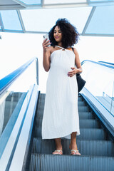 Smiling woman with curly hair browsing smartphone on escalator