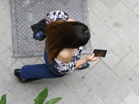 Mujer joven caminando y consultando su tel&eacute;fono m&oacute;vil vista desde arriba en perspectiva cenital a&eacute;rea