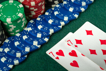 Obraz premium Multi-colored casino chips are neatly stacked next to a pair of sevens cards, indicating an active card game taking place in a lively setting