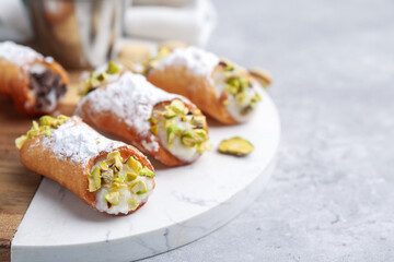 Delicious cannoli with ricotta cheese, pistachios and powdered sugar on grey marble table, closeup. Space for text
