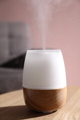 One stylish aroma lamp on wooden table against pink wall, closeup