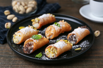 Delicious cannoli with cheese, nuts, powdered sugar, chocolate and mint on wooden table, closeup
