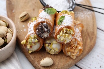 Delicious cannoli with cheese, nuts, powdered sugar, chocolate and mint on white wooden table, closeup