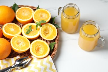 Freshly squeezed orange juice, fruits and juicer on white table