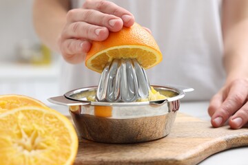 Making juice. Woman with orange using juicer at table indoors, closeup
