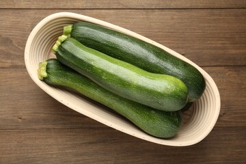 Fresh ripe zucchinis in wicker basket on wooden table, top view