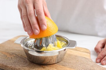 Making juice. Woman with orange using juicer at table indoors, closeup