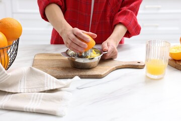 Making juice. Woman with orange using juicer at white marble table indoors, closeup