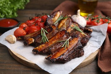 Roasted beef ribs with spices and tomatoes on wooden table, closeup