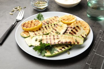 Delicious grilled courgette slices with pumpkin seeds, lemon and parsley on grey table, closeup