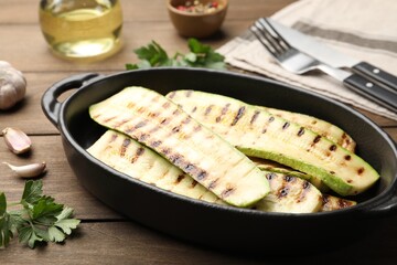 Delicious grilled courgette slices in baking dish and parsley on wooden table, closeup