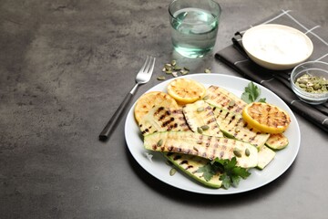 Delicious grilled courgette slices with pumpkin seeds, lemon and parsley on grey textured table, closeup