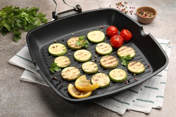 Delicious grilled courgette slices with tomatoes, lemon and parsley in pan on grey textured table, closeup