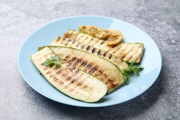 Delicious grilled courgette slices with parsley and lemon on gray textured table, closeup