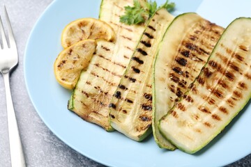 Delicious grilled courgette slices with parsley and lemon served on gray table, closeup