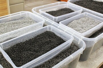 Clear Plastic Containers Filled with Granular Material. Transparent Boxes with Small Pellets. Containers Holding Black and Grey Plastic Granulate. Clear Bins with Industrial Black and Grey Granules