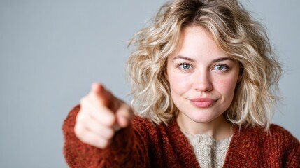 A young woman with curly hair confidently points at the camera while exuding a sense of empowerment and engagement, inviting viewers to participate in her message.