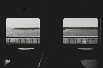 Silhouette of window frame, table and seat in boat with rain and cloudy in dark tone, Ferry public transportation between Texel island and mainland with sea view and dune, Noord Holland, Netherlands