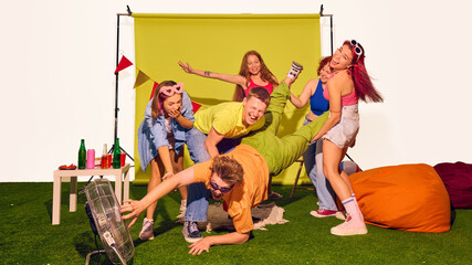 Friends holding one person by legs as he reaches toward fan laughing. Concept of playful teamwork, social media fun, advertising creativity, and carefree youth energy.