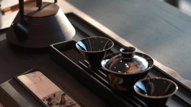 Black glazed ceramic tea set including teapot and tea tray arranged on wooden surface in still life composition