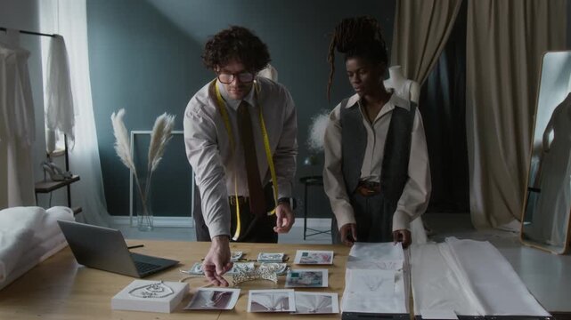 Two diverse male and female fashion designers working on new wedding dress, using visual references and choosing fabric