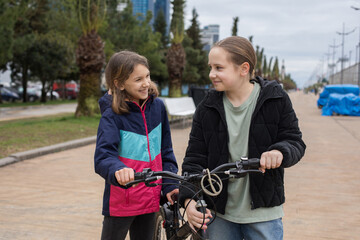 Joyful children girls 10 and 12 years old with bicycle walking outdoors