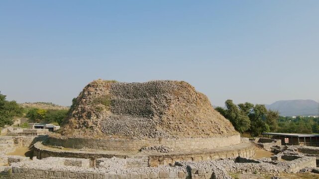 Aerial view of Dharmarajika Stupa's ancient stone remains under a clear sky, contrasting textures of stone and dry grass, Taxila, Punjab, Pakistan.