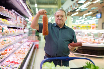 Elderly man chooses sausage in supermarket