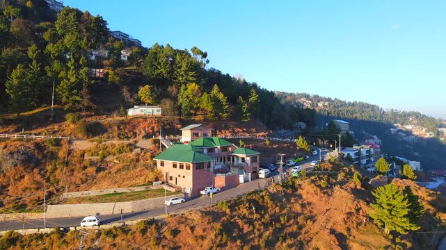 Aerial view of buildings with green roofs nestled amongst trees and roads winding through the hilly terrain, Murree, Punjab, Pakistan.
