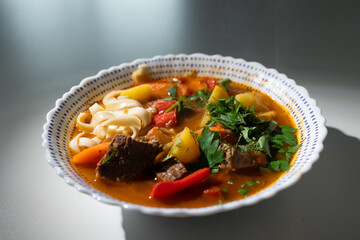 A hearty bowl of lagman soup showcases tender meat, vibrant vegetables, and fresh herbs, creating a filling and savory meal. The dish features noodles and rich broth, perfect for satisfying cravings.