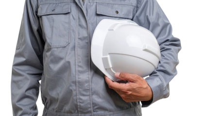 A worker wearing gray coveralls holding a white hard hat at chest level, representing construction safety and personal protective equipment.