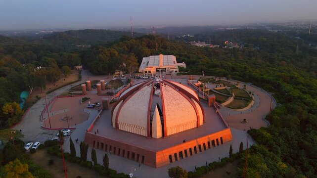 Aerial view of the Pakistan Monument basking in the warm glow of the setting sun, surrounded by lush green trees and winding pathways, Islamabad, Islamabad Capital Territory, Pakistan.