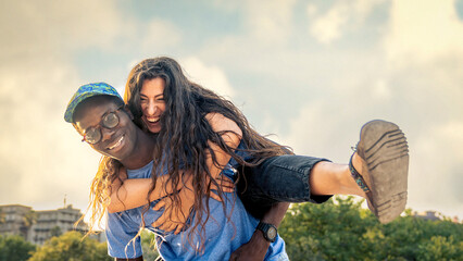 Happy multicultural couple of young adults, smiling woman hugging African man with glasses, enjoying summer lifestyle and outdoor fun; concept of diversity, joy, freedom and carefree happiness