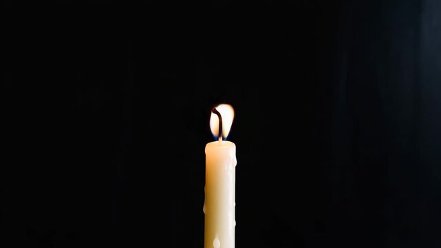 Simple candle with bright flame burning in black background, symbolizing hope, light and warmth.