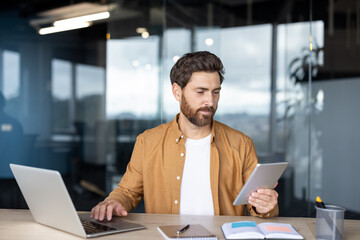 Focused businessman working with laptop and digital tablet in modern office