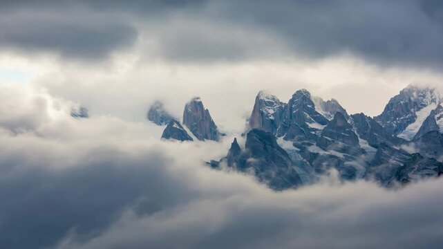 Dark sharp mountain peaks breaking through thick clouds in dramatic alpine weather, creating wild and remote atmosphere.