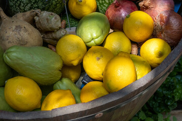 Assorted organic vegetables and fruits shown on a market, including lemon, chayote, onion and etc