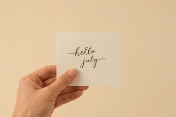 Hand holding July greeting card, beige background