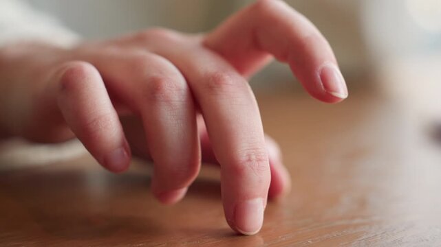 Close up hand of white person in white sleeve slowly tapping wooden table with finger during thoughtful moment in soft natural indoor light expressing calm, reflection