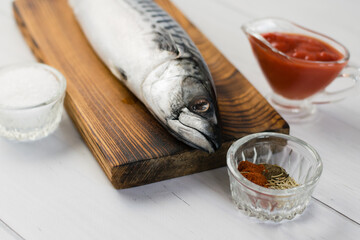 Raw mackerel fish on a cutting board, cooking fish with salt, spices and sauce