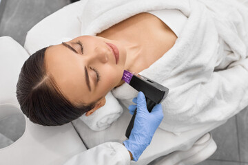 Fototapeta na wymiar Beautiful woman enjoys while microneedling RF lifting for her neck and body skin tightening with cosmetologist at beauty salon