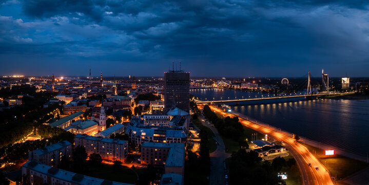 Night view of Riga, Latvia, featuring the illuminated Vansu Bridge over the Daugava River, the Riga TV Tower, and the Latvian Academy of Sciences.