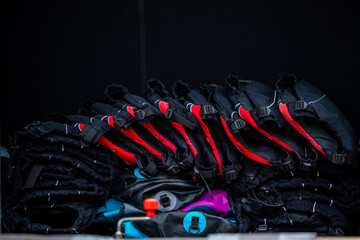 Neatly arranged life jackets in black and red with blue and purple accents, layered in order. A...