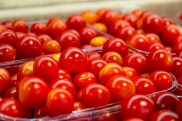 Close-up Small red cherry tomatoes are lying in transparent trays on the shop counter. Tomato theme background