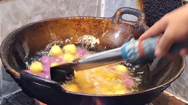 A street vendor is frying sweet potato balls, known as bola ubi, in hot oil.