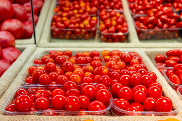 Small red cherry tomatoes are lying in transparent trays on the shop counter. Tomato theme background